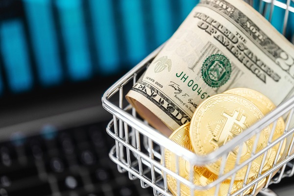 Dollar bill and gold Bitcoin coins inside a small shopping basket on a keyboard