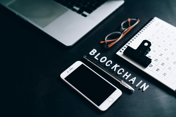Wooden letter tiles spelling blockchain next to a smartphone and calendar on a desk
