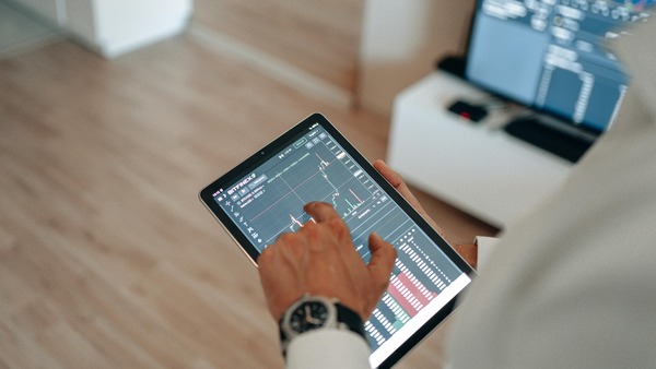 Hand holding a tablet displaying a cryptocurrency trading chart and wallet balance