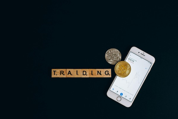 Smartphone showing a bitcoin price chart next to wooden tiles spelling trading