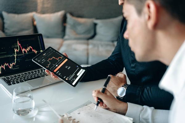 Trader analyzing multiple computer monitors showing cryptocurrency price charts while holding a tablet
