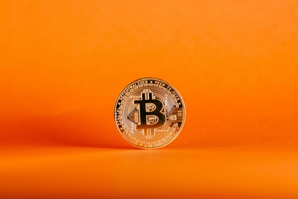 Gold Bitcoin-style cryptocurrency coin standing on a bright orange background