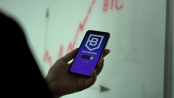 Wooden tiles spelling trading next to a smartphone showing a cryptocurrency chart and coins