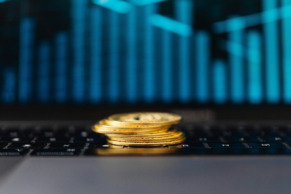 Stack of gold cryptocurrency coins on a laptop keyboard with a blue trading chart in the background