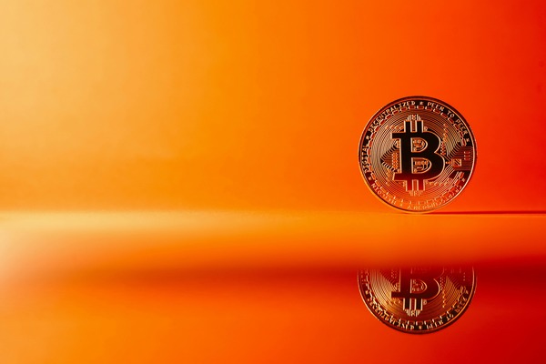 Gold Bitcoin-style cryptocurrency coin standing on an orange reflective surface