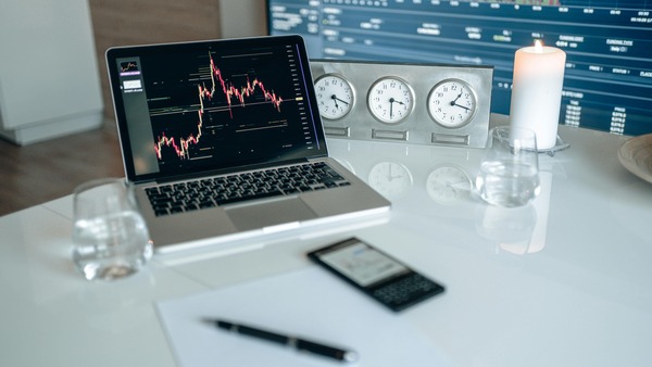 Laptop screen showing a cryptocurrency trading chart next to clocks and a candle